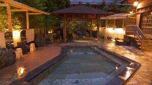A hot spring area with stone flooring, wooden benches, and a covered seating area. - Atami Sekitei (Atami)