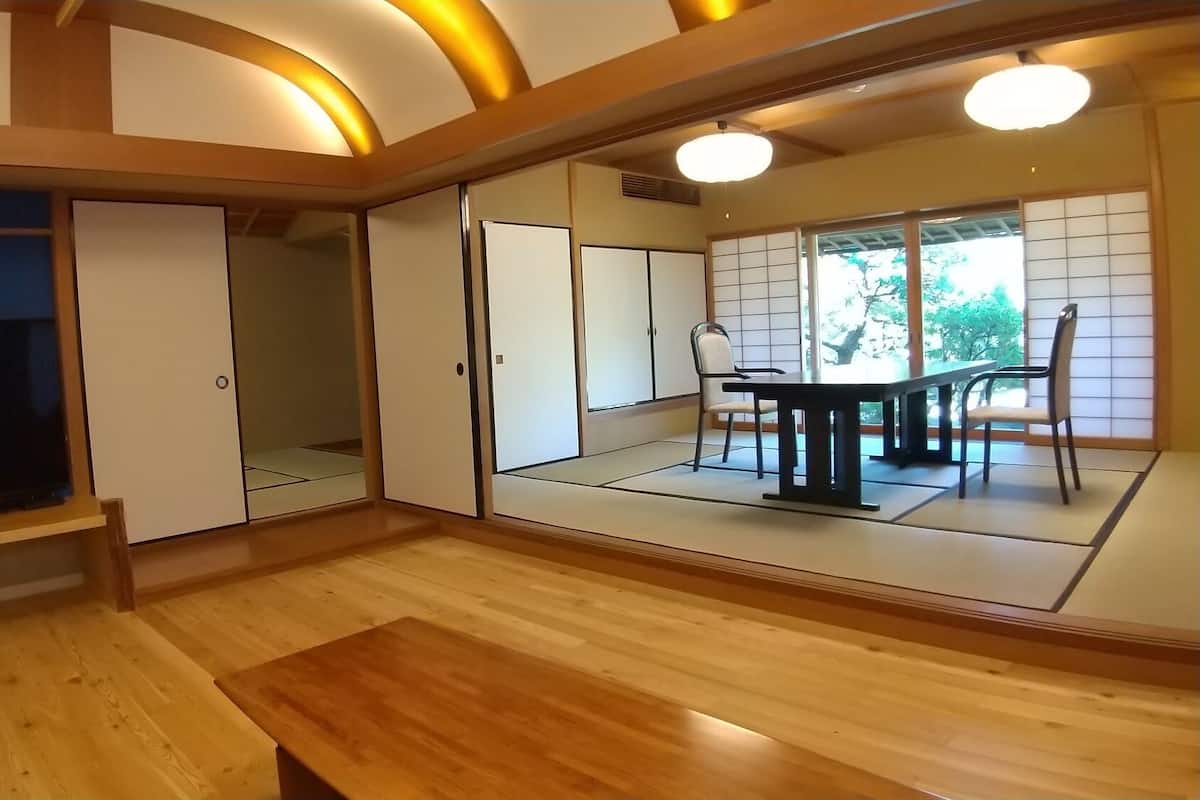 Quarto com televisão, portas de correr, mesa de jantar com cadeiras e vista para o verde lá fora.