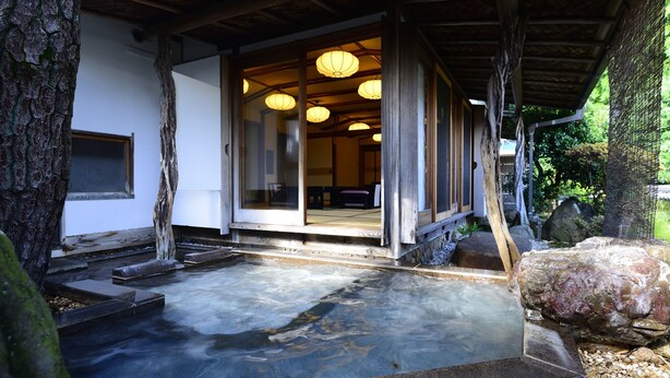 A traditional Japanese onsen with a wooden deck, stone steps, and a view of the interior through glass doors. - Atami Sekitei (Atami)