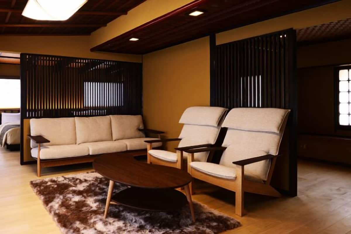 Uma sala de estar tradicional japonesa, com tatames, uma mesa de madeira baixa e um sofá.