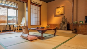 Ett traditionellt japanskt rum med tatamimattor på golvet, ett lågt bord, en stol och ett stort fönster med shojiskärmar.