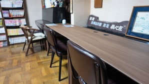 A long wooden table with chairs, a bookshelf with magazines, and a framed picture on the wall. - Yudanaka Onsen Andaikan (Yamanouchi)