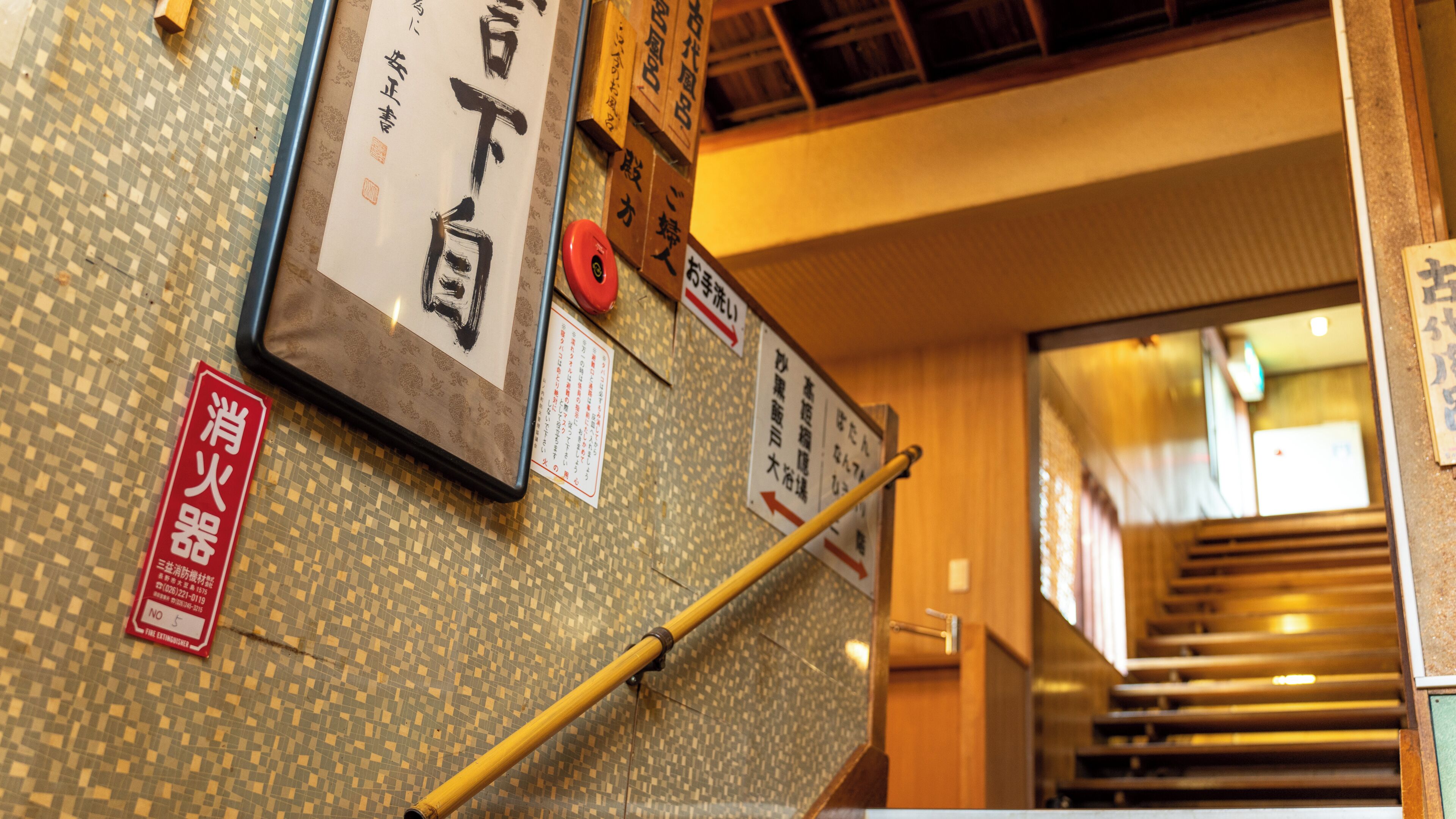 A staircase with signage in Japanese, a fire extinguisher, and a bamboo handrail.