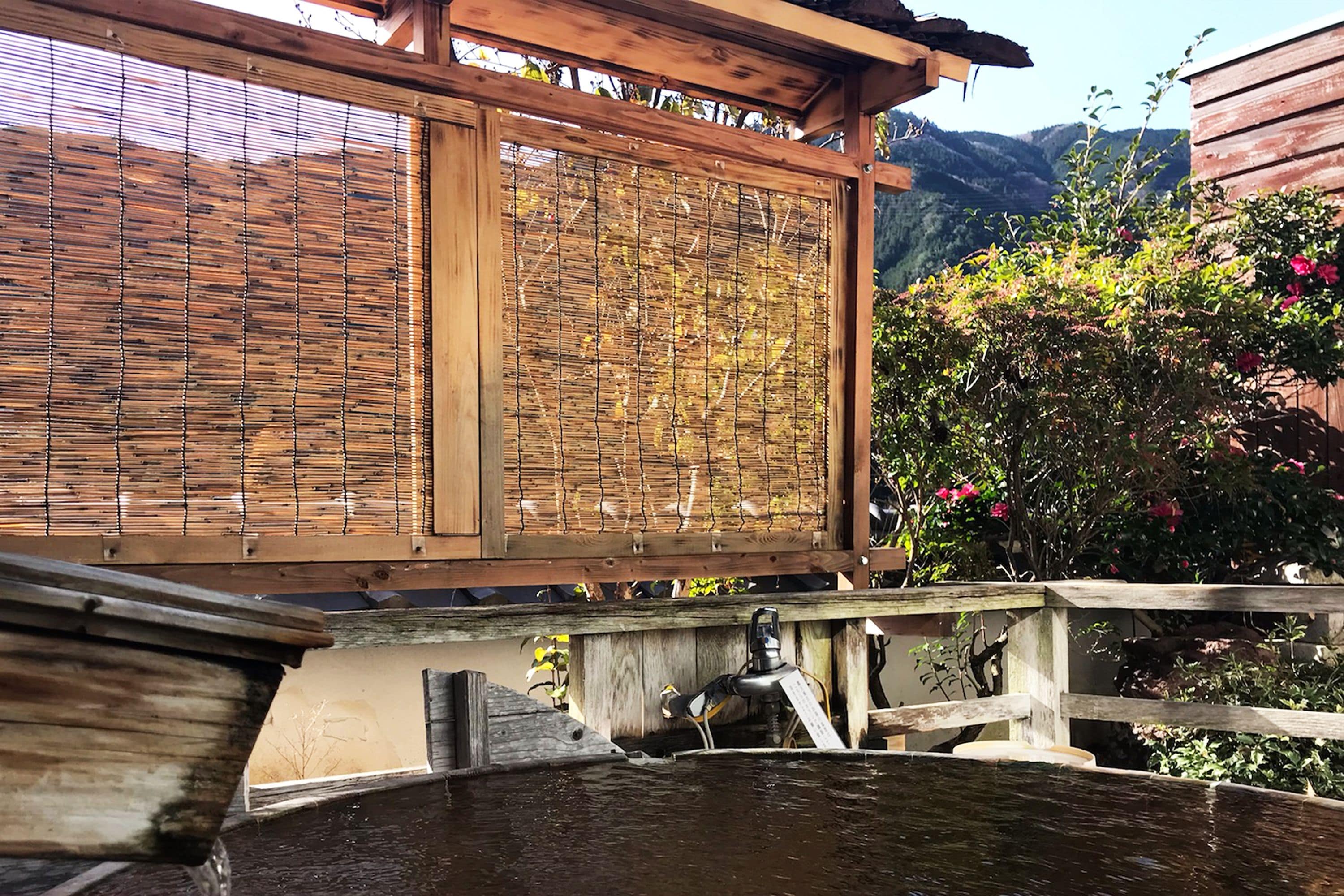 A traditional wooden structure with a bamboo screen, a wooden deck, and a water feature.