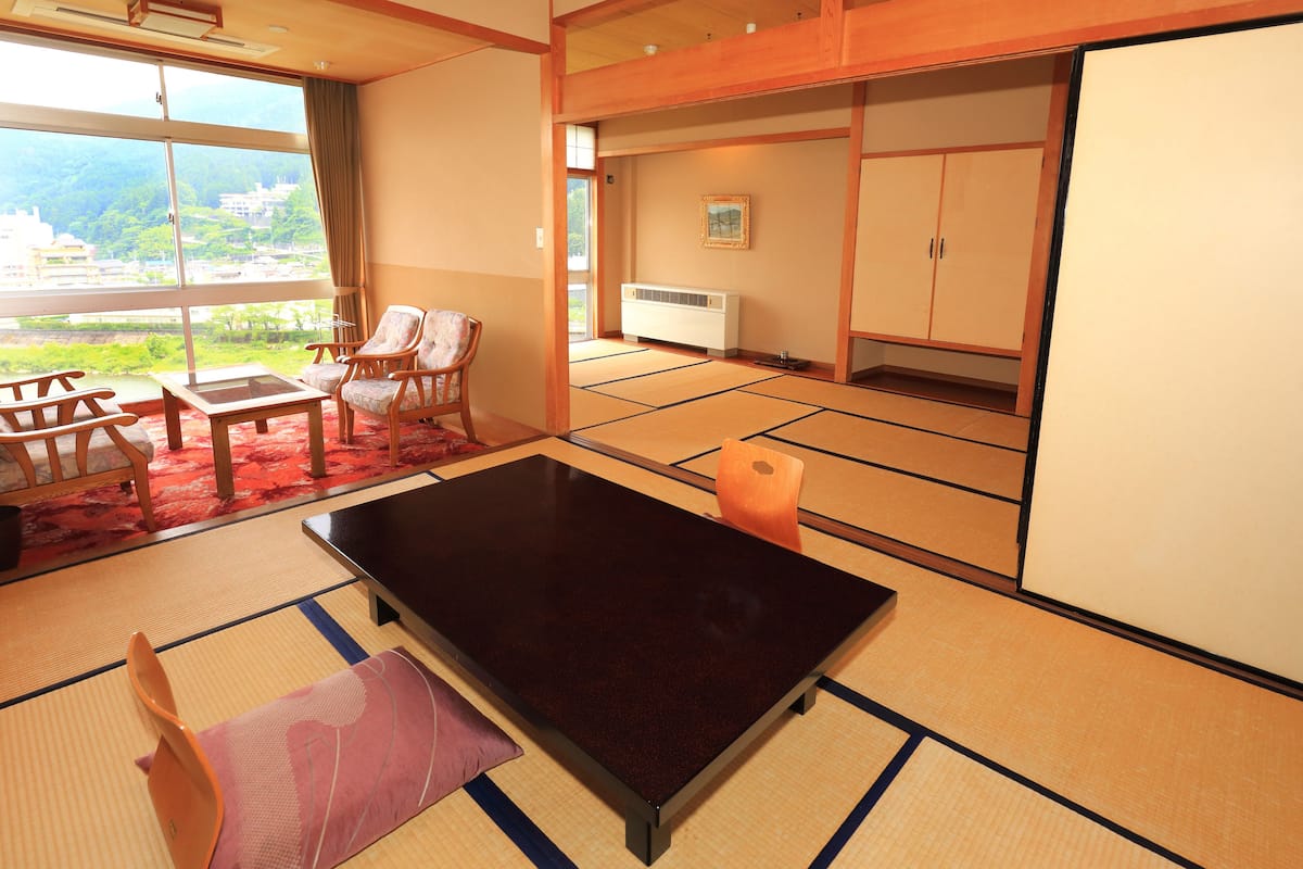 Una habitación japonesa tradicional con suelo de tatami, una mesa baja de tatami y vistas a un paisaje montañoso a través de amplios ventanales.
