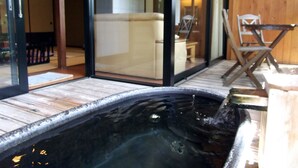 Zona de hidromasaje con terraza de madera, sofá y sillón visibles a través de puertas de cristal.