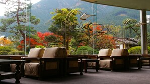 Una habitación tradicional japonesa con suelo de tatami, una mesita baja y vistas a un paisaje montañoso a través de amplias ventanas.