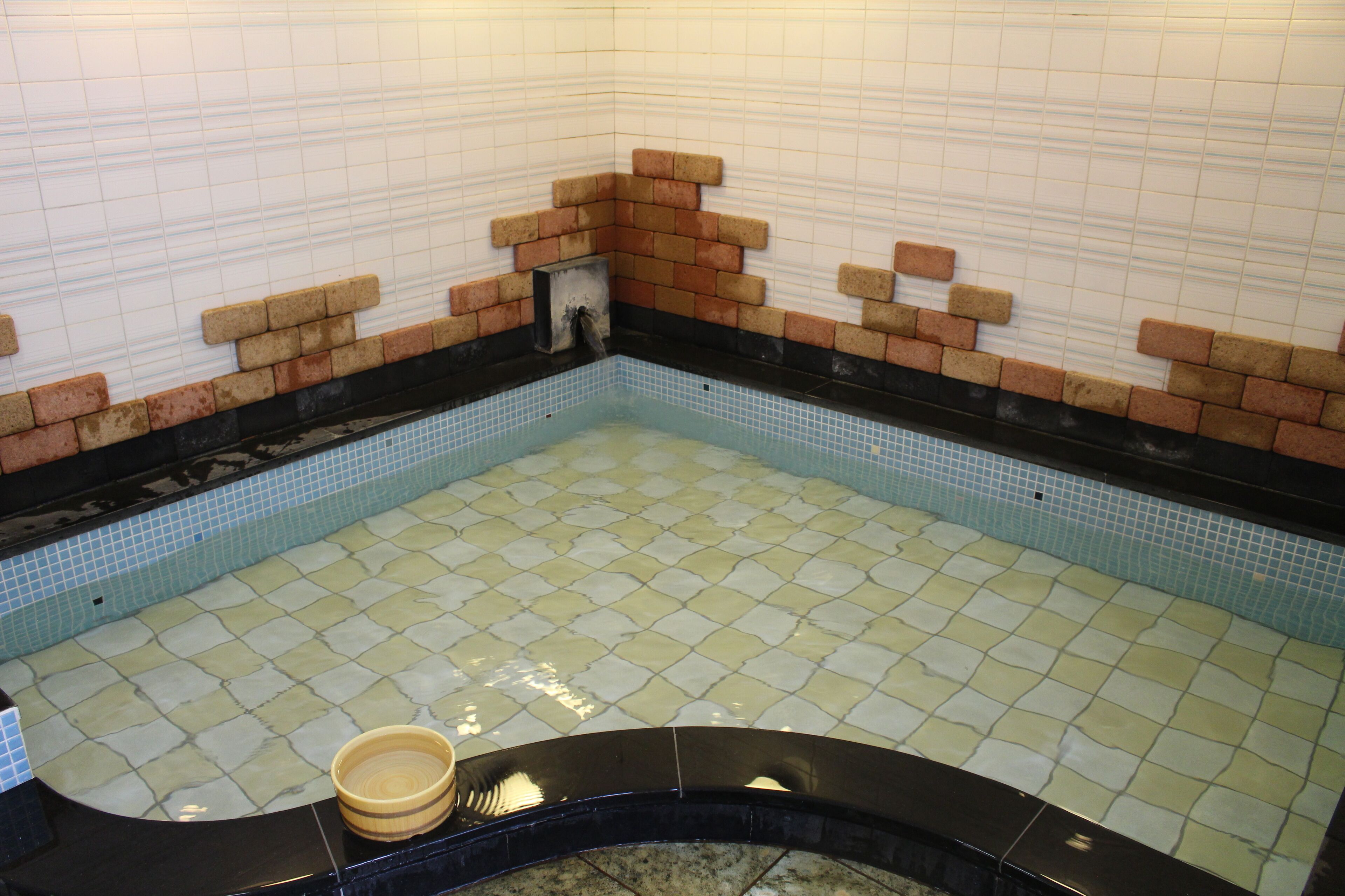 A small pool with tiled walls and floor, a brick accent wall, and a yellow bucket.