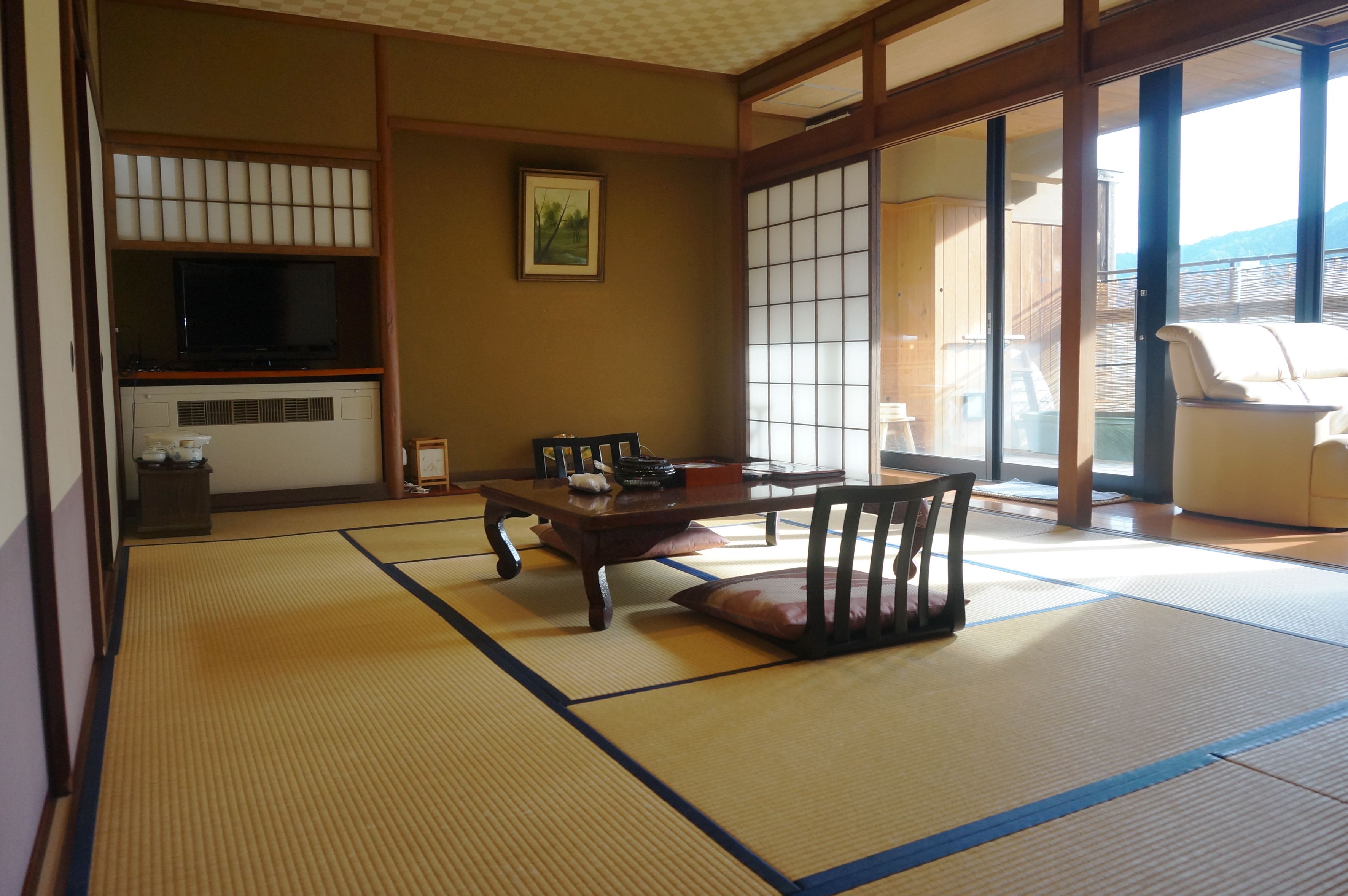 A traditional Japanese room with tatami flooring, a low table, and a sliding door leading to a balcony.