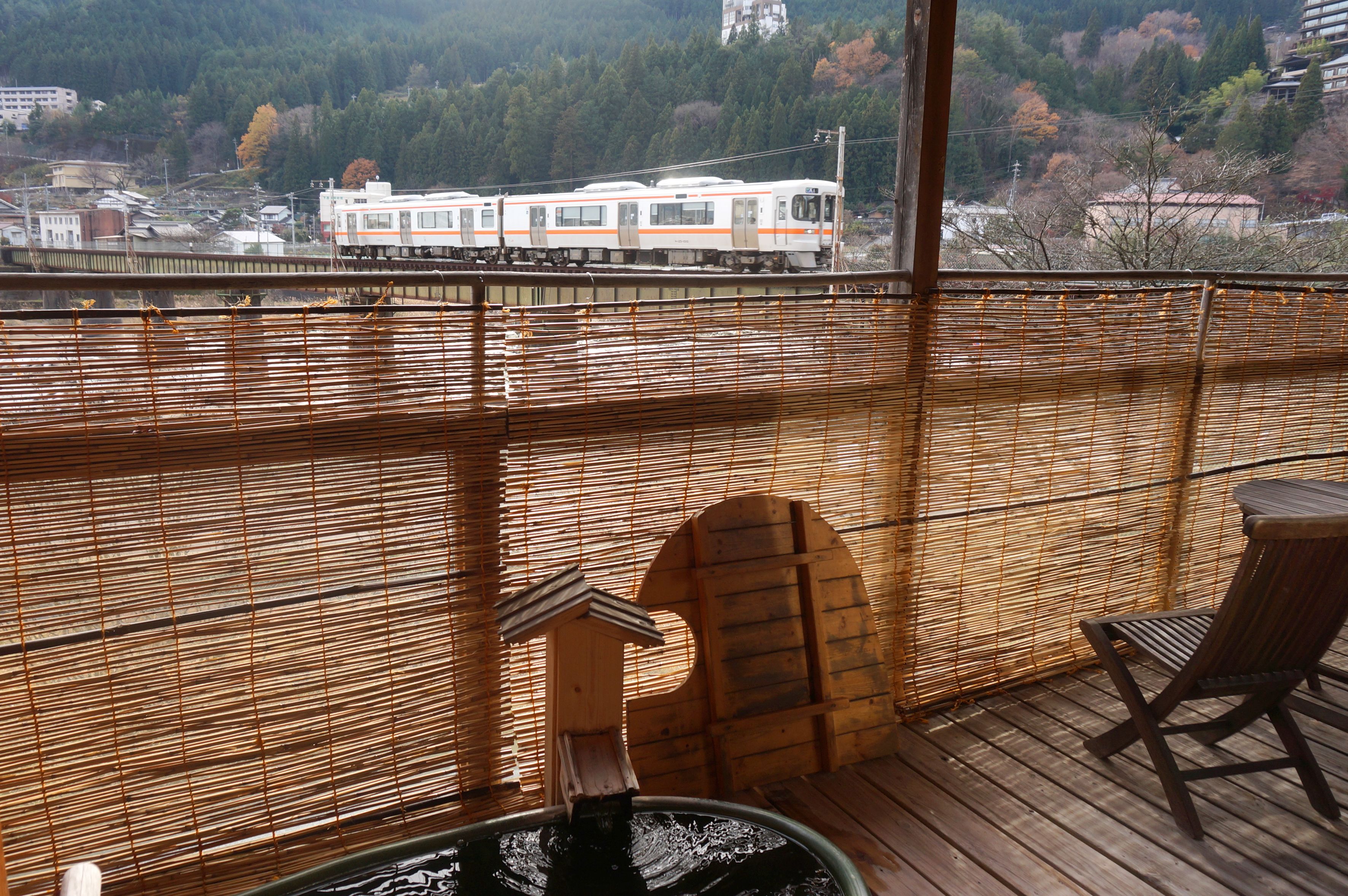 A wooden deck with a hot tub, a wooden chair, and a view of a train passing by.