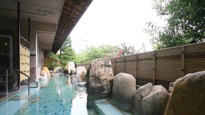 Una piscina con rocas grandes, una cerca de madera y un edificio con fachada de azulejos.