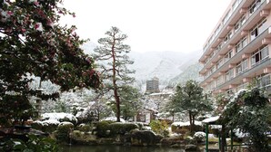 Un jardín japonés tradicional con un estanque, rocas y plantas cubiertas de nieve.