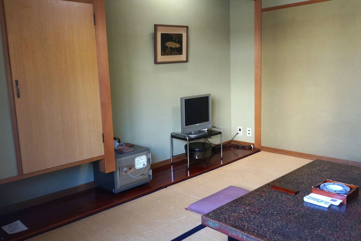 Una habitación con un armario de madera, un televisor sobre un soporte, un calentador pequeño y una mesa con un control remoto.