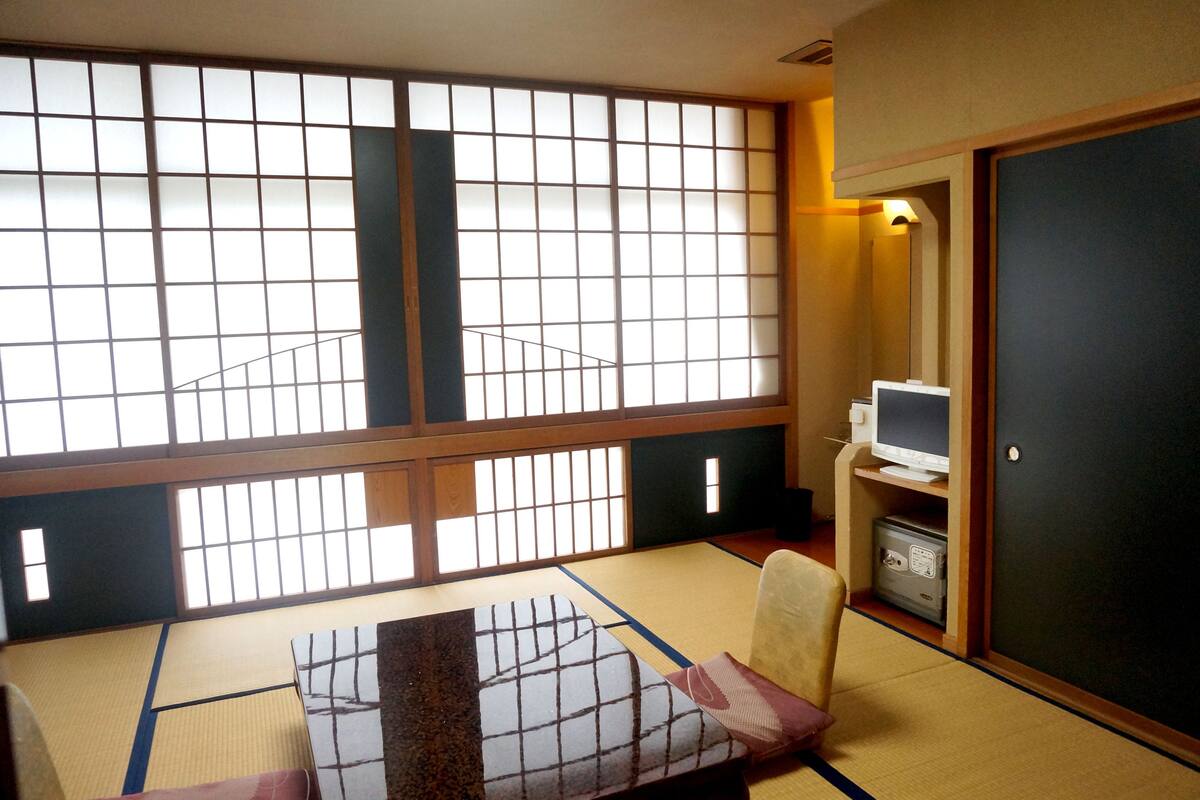 Una habitación con suelo de esterillas de tatami, una cama futón, un televisor y un puertas correderas tradicionales.