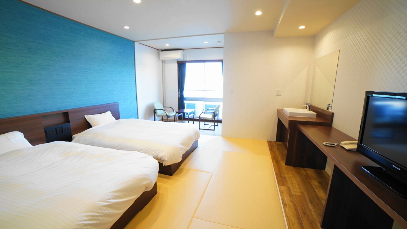 Habitación de hotel con dos camas, un escritorio con televisor, baño y vista al exterior.
