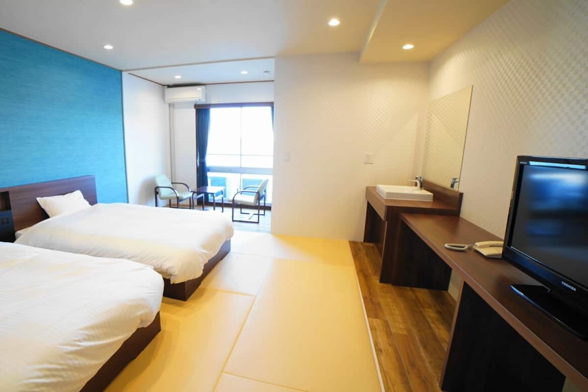 A hotel room with two beds, a desk with a TV, a bathroom, and a view of the outside.