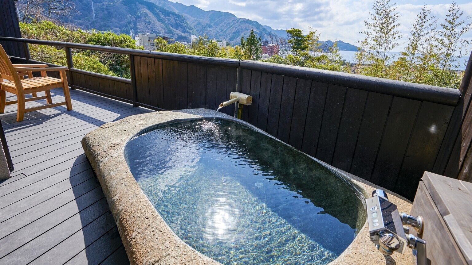 Een hottub op een houten terras met uitzicht op bergen en een wateroppervlak.