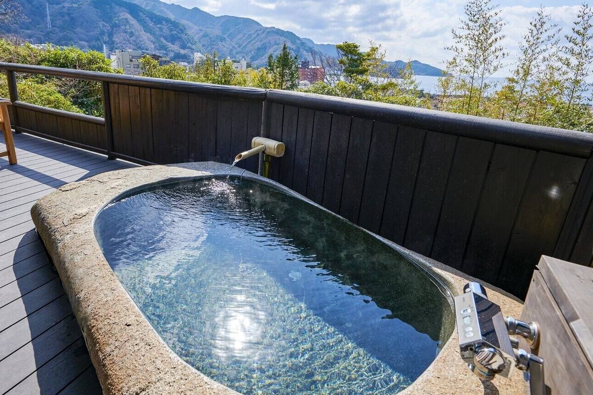 Un bain à remous sur une terrasse en bois, avec vue sur les montagnes et un plan d’eau.
