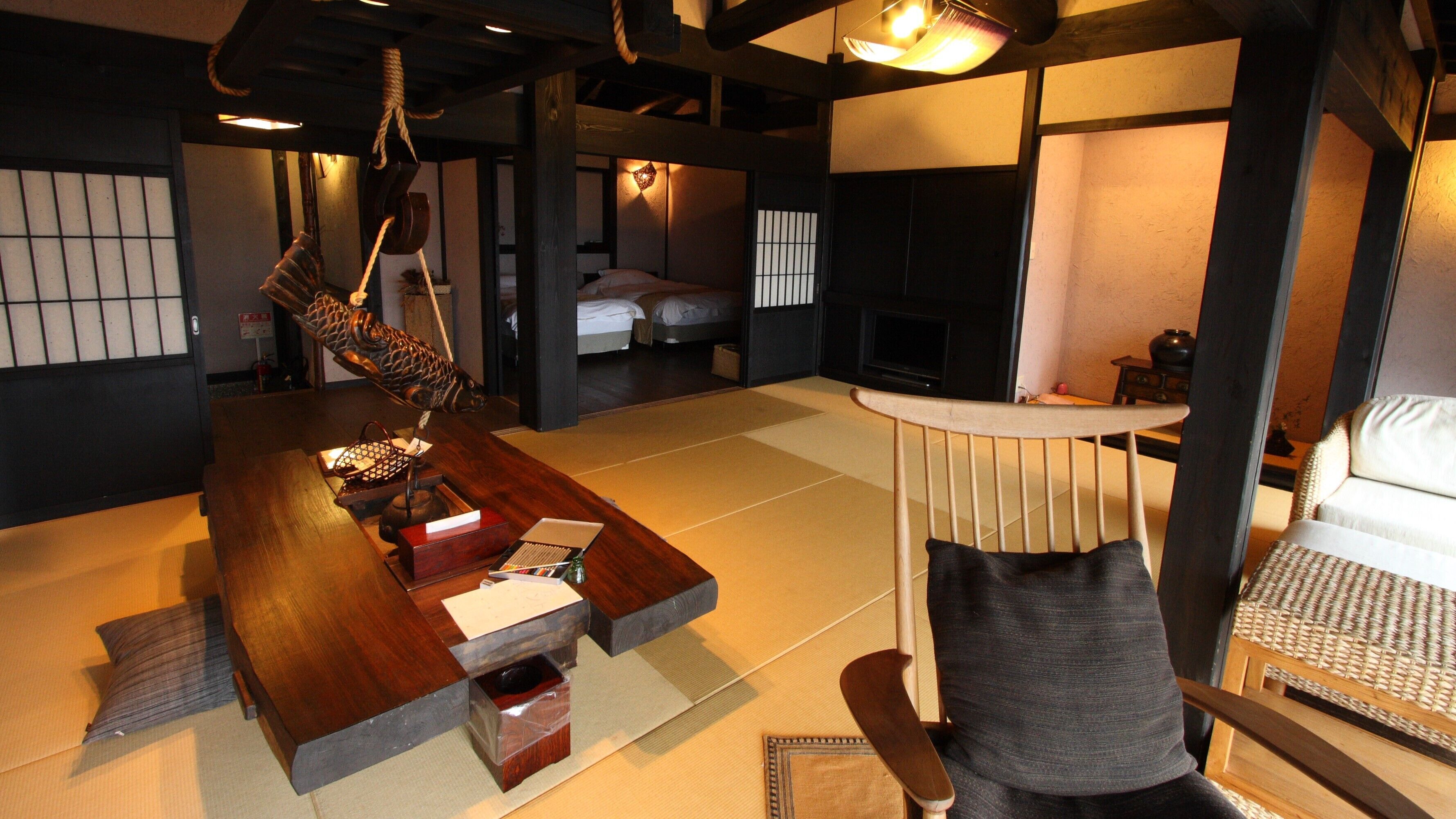 Een traditionele Japanse kamer met tatami vloeren, een lage houten tafel, een hangende sculptuur van een vis en een bank met een geweven kussen.