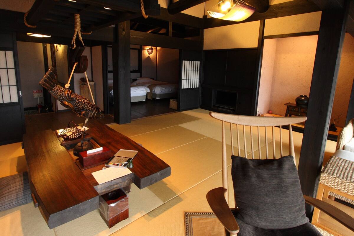 Une pièce de style japonais traditionnel, avec un sol recouvert de tatamis, une basse table en bois, une sculpture de poisson suspendue et un canapé agrémenté d’un coussin tissé.