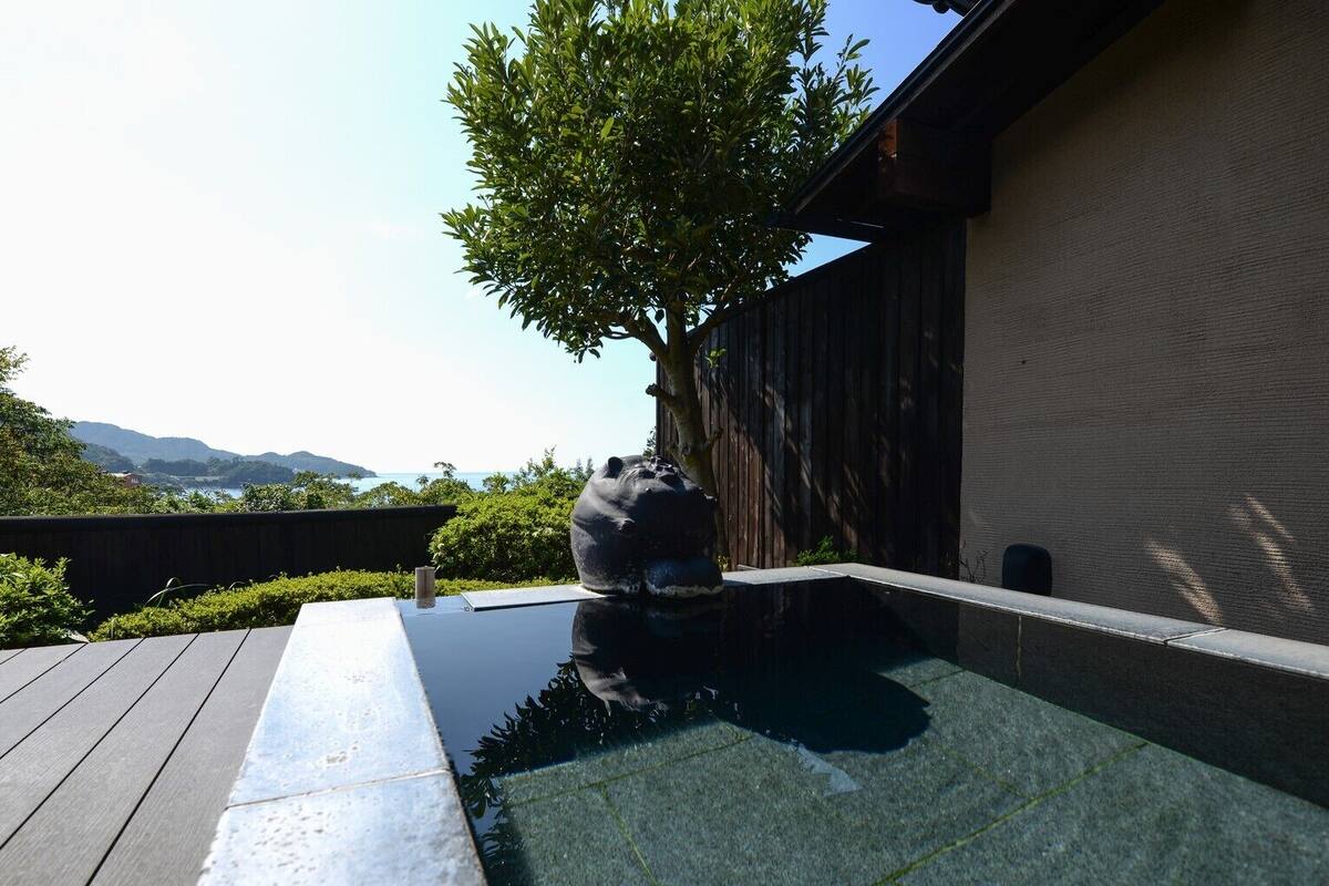 Un bâtiment moderne doté d’une terrasse en bois, d’un arbre et offrant une vue sur la mer et les montagnes.