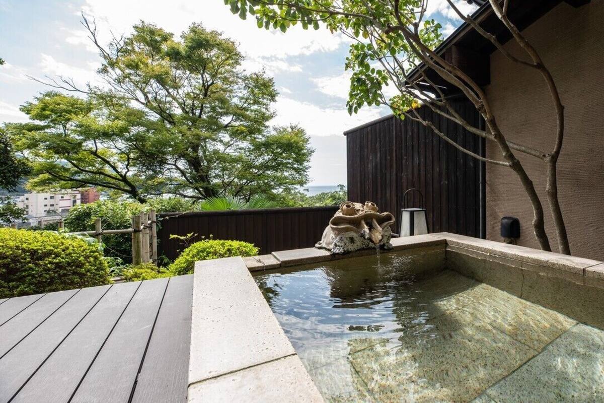Un espace de sources chaudes doté d’une terrasse en bois, d’un bassin en pierre et d’un bâtiment à l’extérieur sombre.