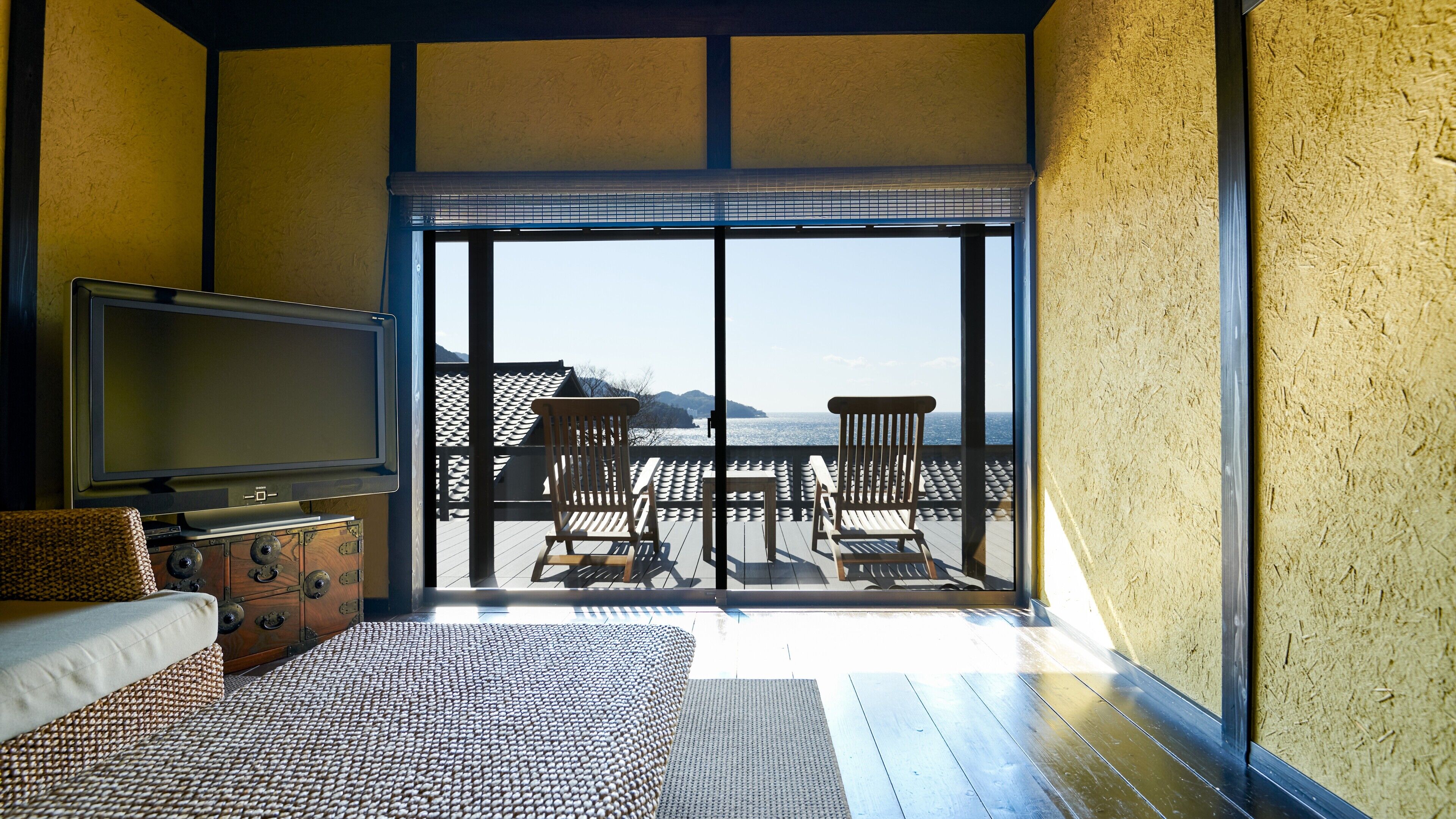 Een kamer met een bed, een televisie, een houten kist en een balkon met stoelen en een tafel.