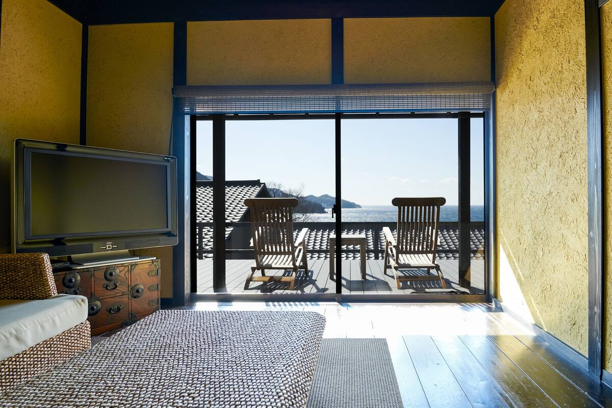 Une chambre avec un lit, une télévision, une commode en bois et un balcon équipé de chaises et d’une table.