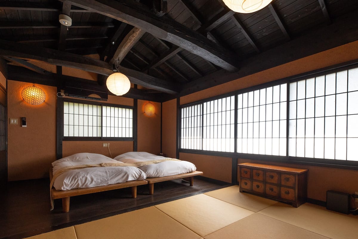 Una habitación tradicional japonesa con suelo de tatami, una cama de madera, un aparador y ventanas amplias con diseños de cuadrícula.