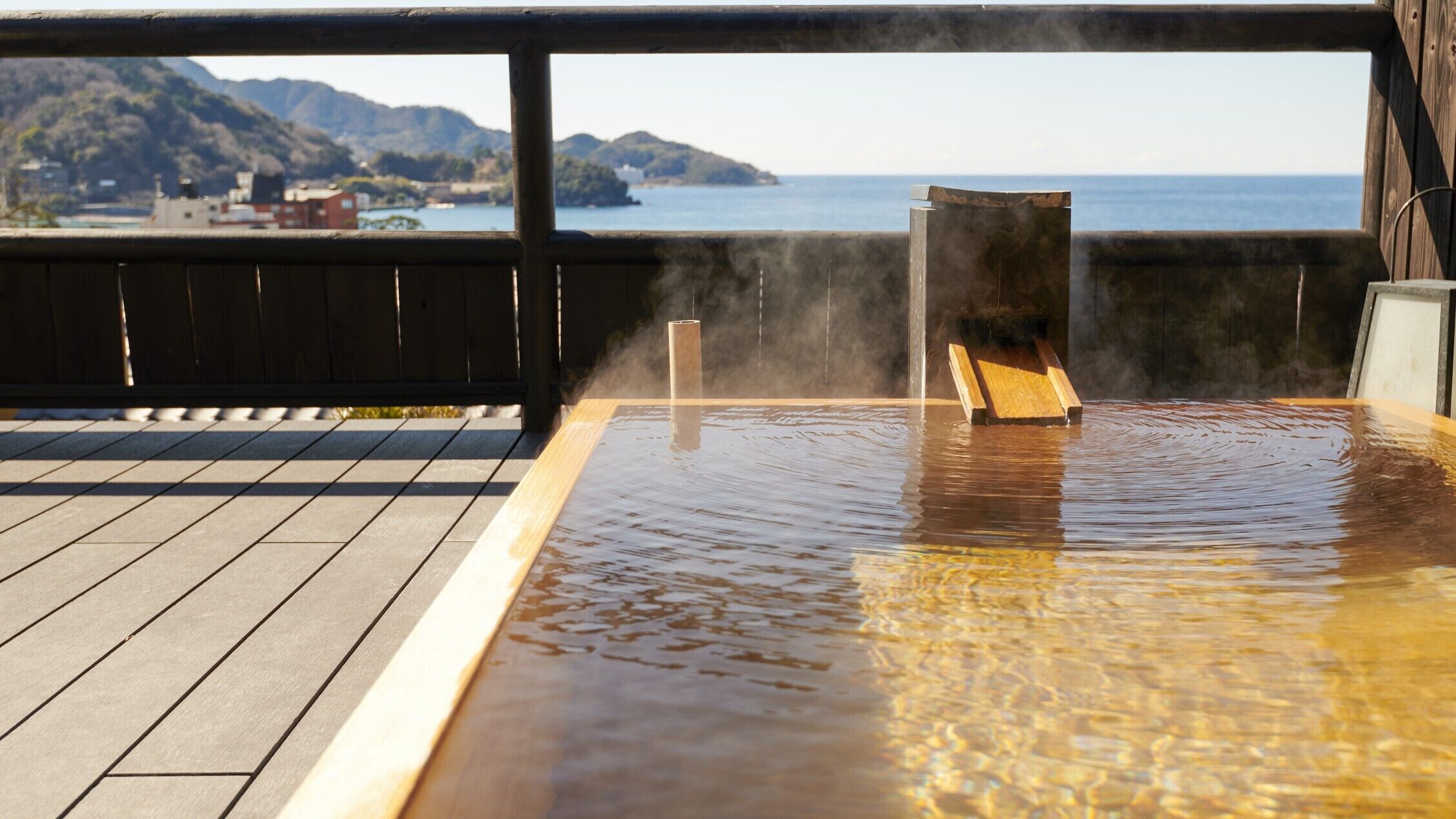 Een warmwaterbronbad met een houten terras en uitzicht op zee en bergen.