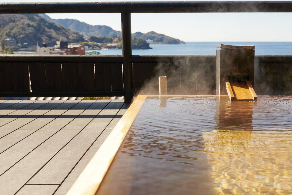 Un bain thermal en plein air, avec une terrasse en bois et une vue sur la mer et les montagnes.