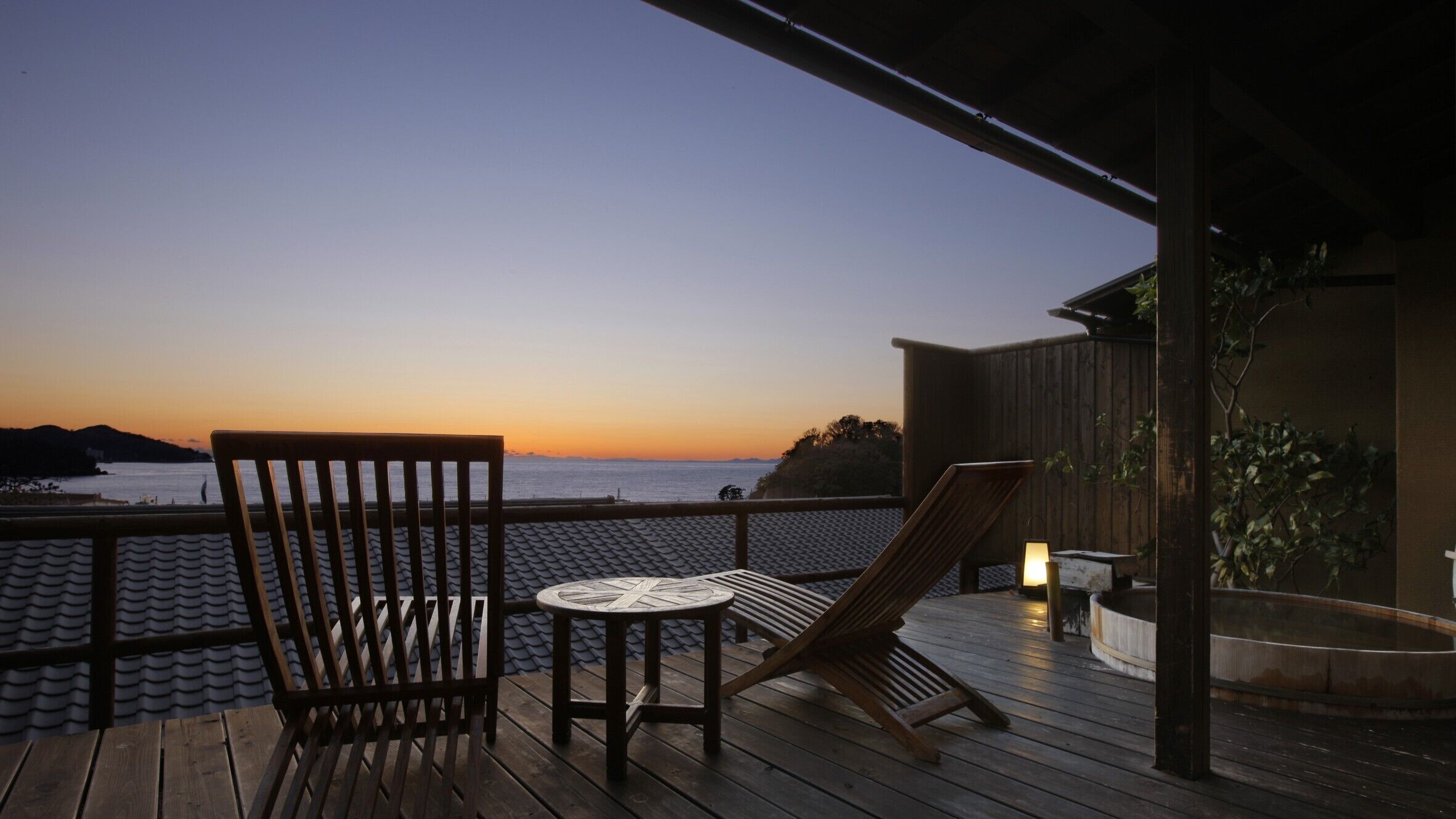 Een houten terras met een tafel en stoelen, uitkijkend op een wateroppervlak bij zonsondergang.