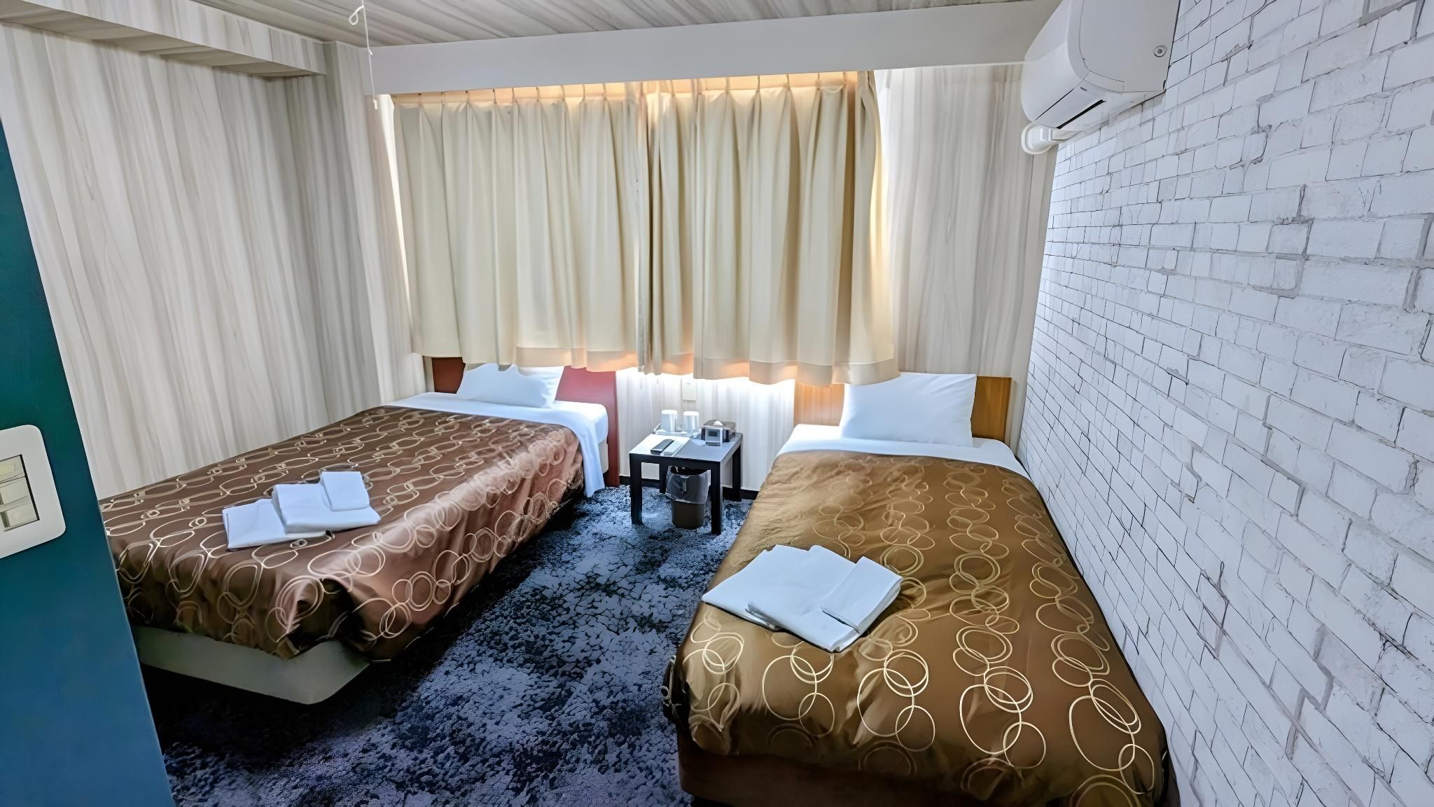 Een hotelkamer met twee bedden, een tafeltje en een raam met gordijnen.