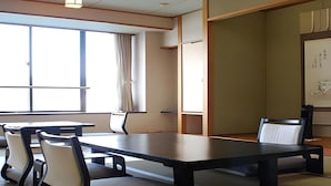 A traditional Japanese-style room with tatami flooring, a low table with chairs, and a large window with curtains.
