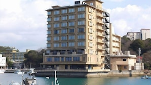 A multi-story hotel with a flat roof, located near a body of water with boats docked.