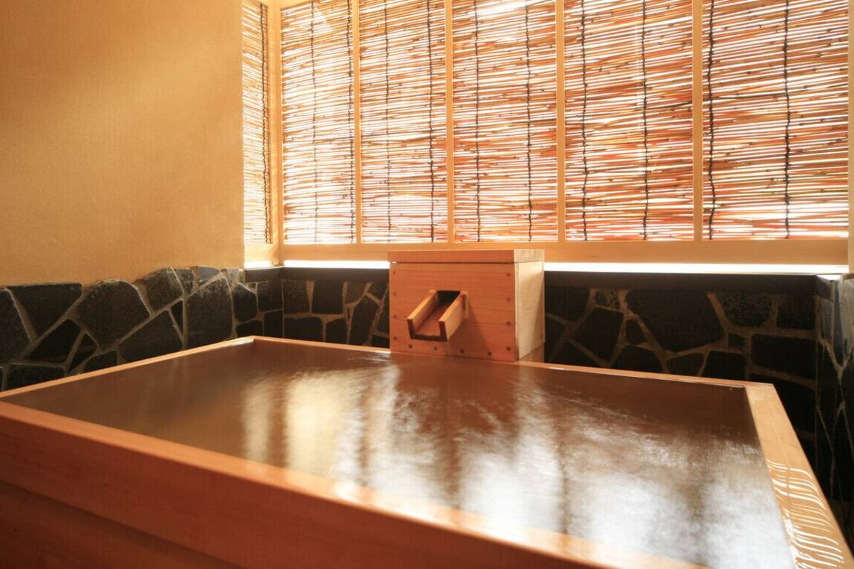 A spa room with a wooden massage table, stone wall, and a window with bamboo blinds.