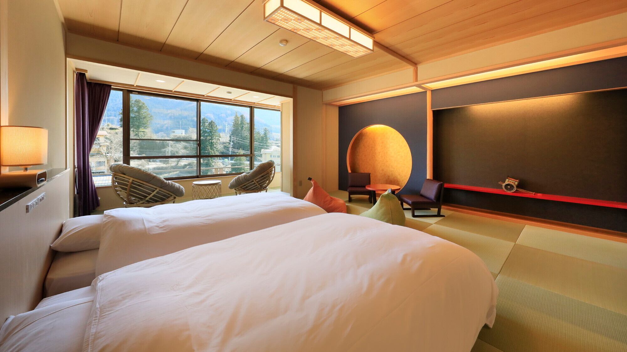Quarto de hotel com duas camas, uma janela grande com vista, uma mesa redonda e uma TV fixada na parede.