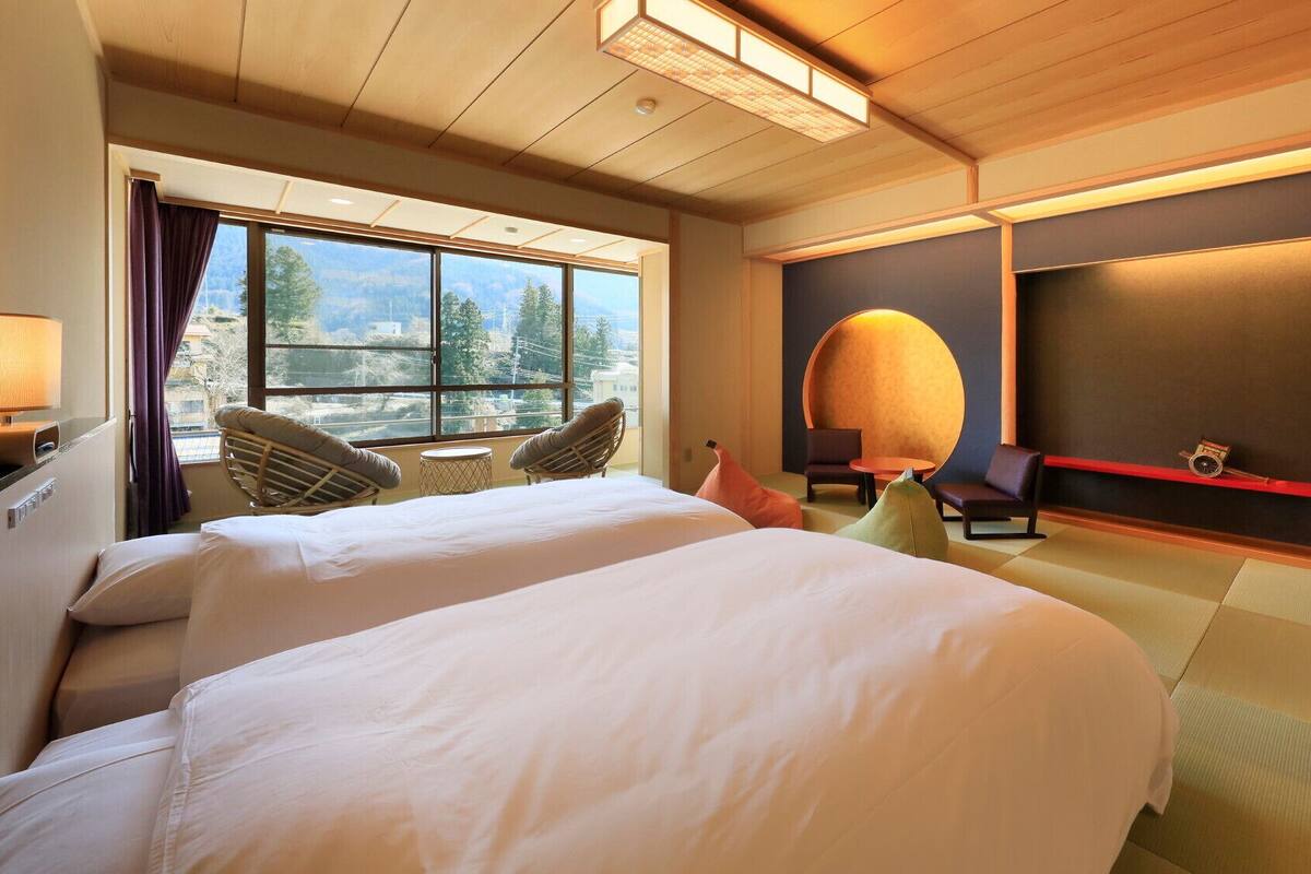 A hotel room with two beds, a large window with a view, a round table, and a wall-mounted TV.