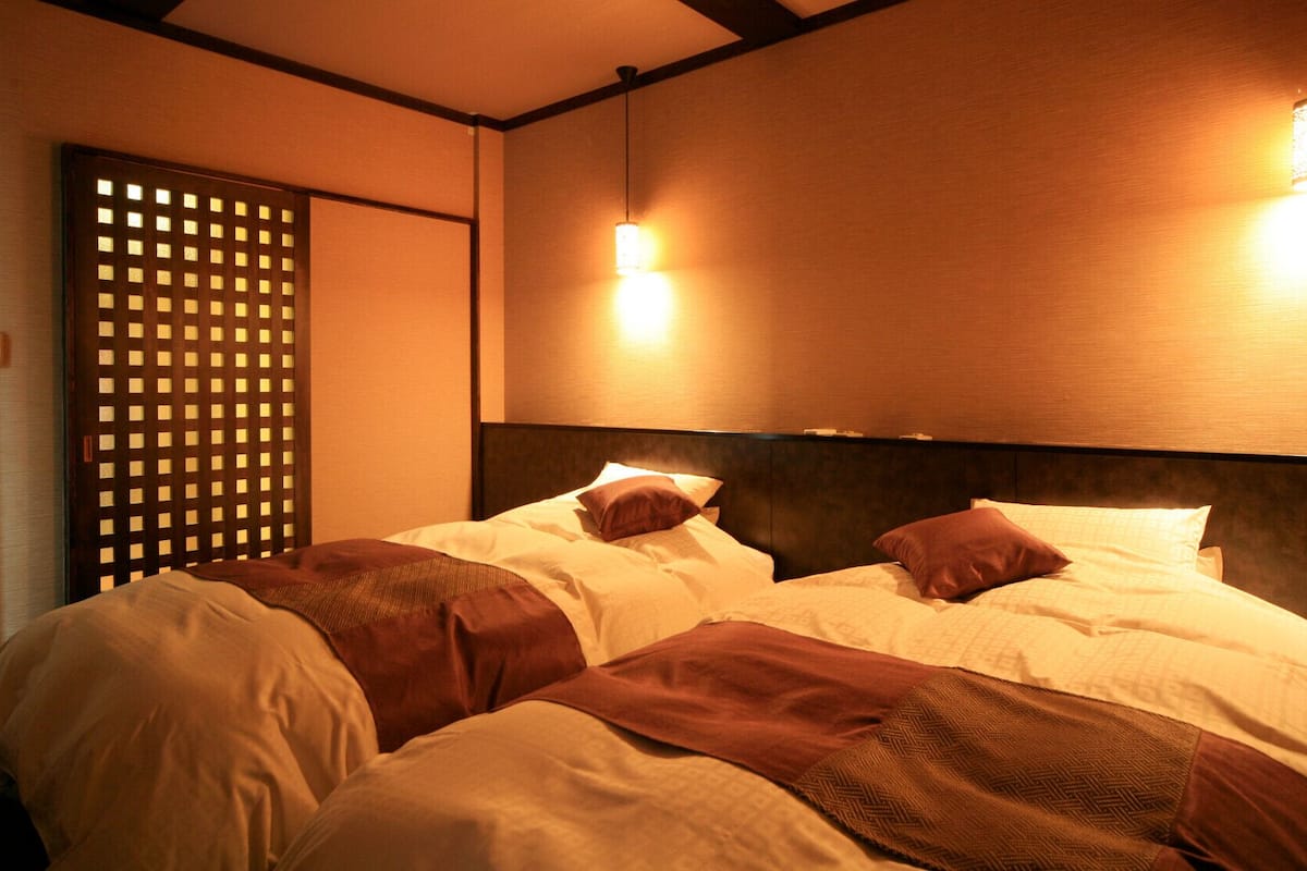 Une chambre d’hôtel avec deux lits, une tête de lit en bois et une porte coulissante à motifs géométriques.