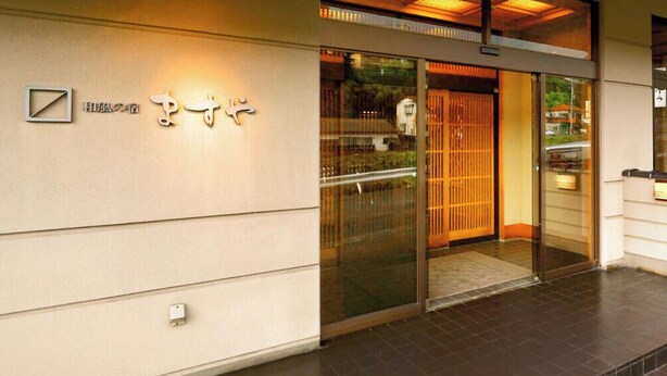 Ein Hotelzugang mit einer Schiebeglastür, einem Schild mit japanischen Schriftzeichen und einem gefliesten Boden.