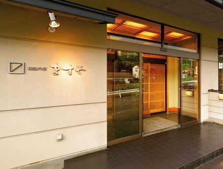 A hotel entrance with a sliding glass door, a sign with Japanese characters, and a tiled floor.