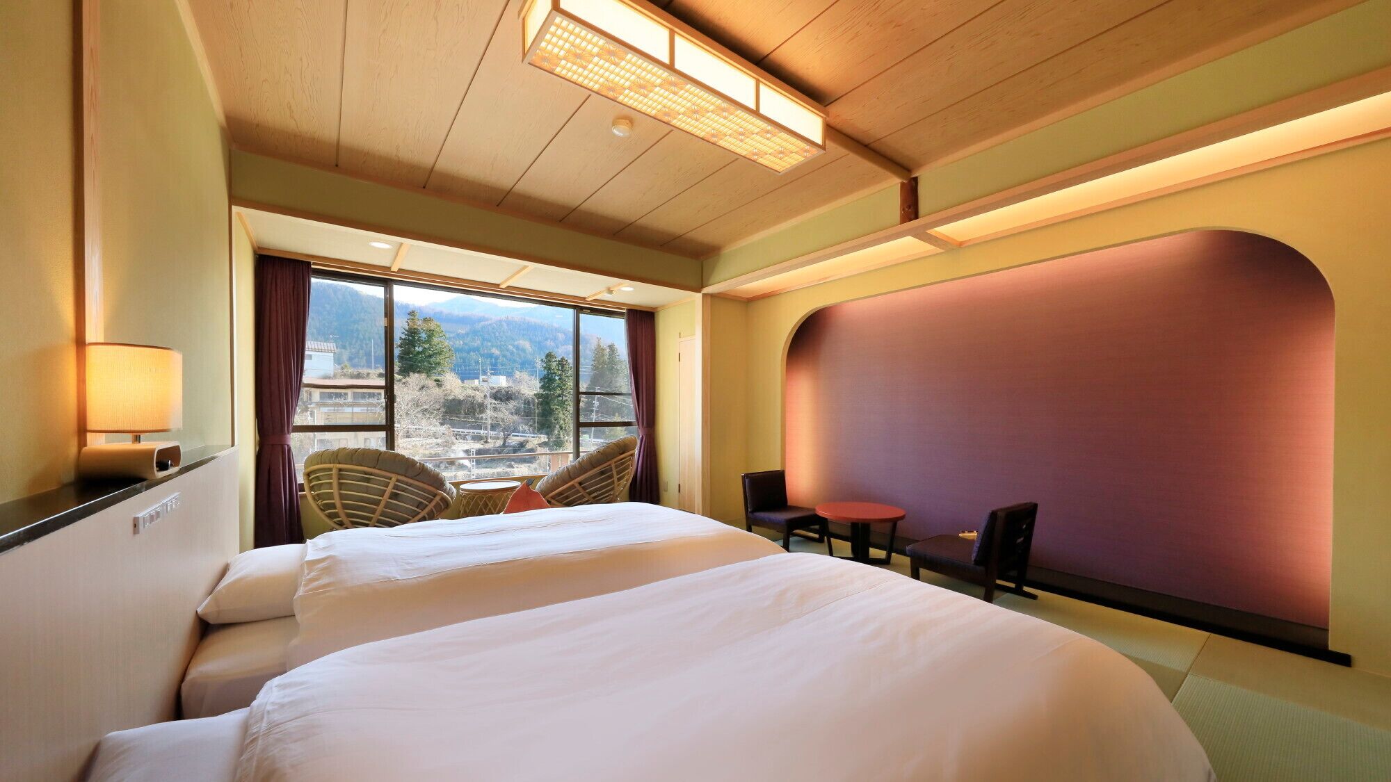 Quarto de hotel com uma cama grande, uma mesa pequena, duas cadeiras, vista da cidade e uma janela ampla.