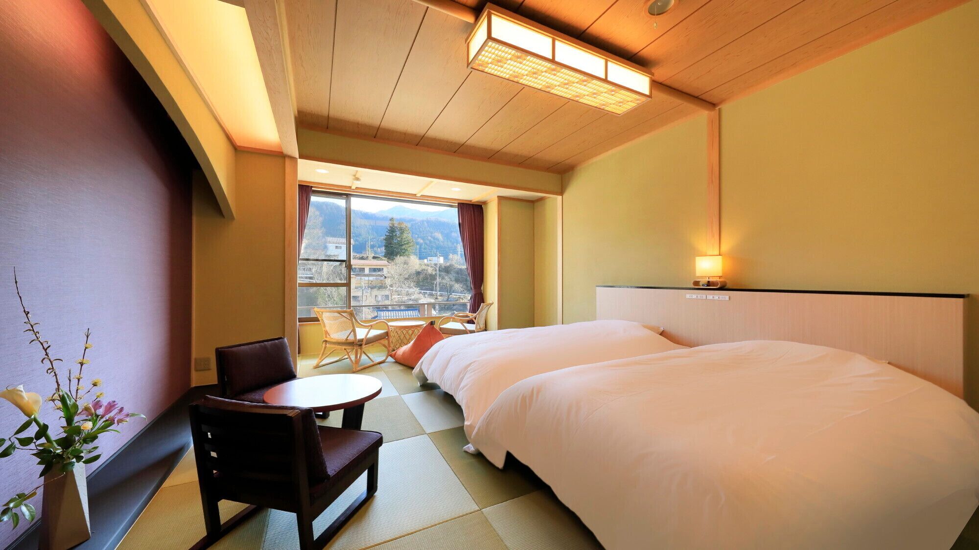 Quarto de hotel com cama, uma cadeira, uma mesinha e vista para as montanhas pela janela.