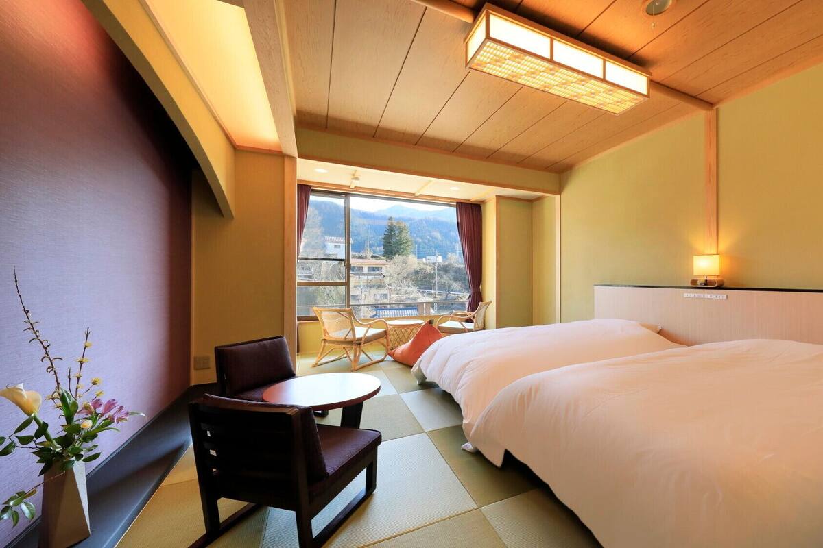 A hotel room with a bed, a chair, a small table, and a view of mountains through the window.