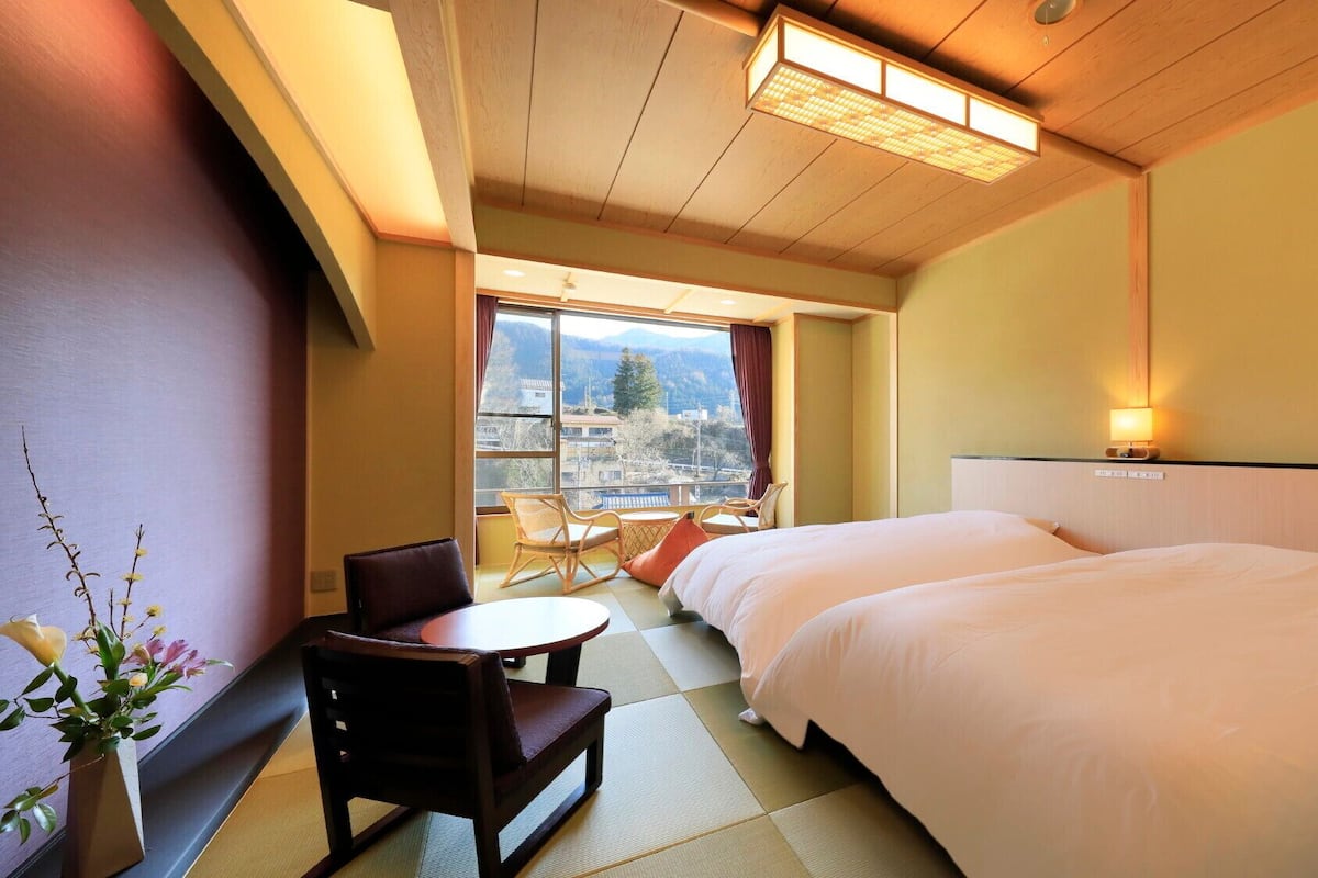Une chambre d’hôtel avec un lit, une chaise, une petite table et une vue sur les montagnes par la fenêtre.