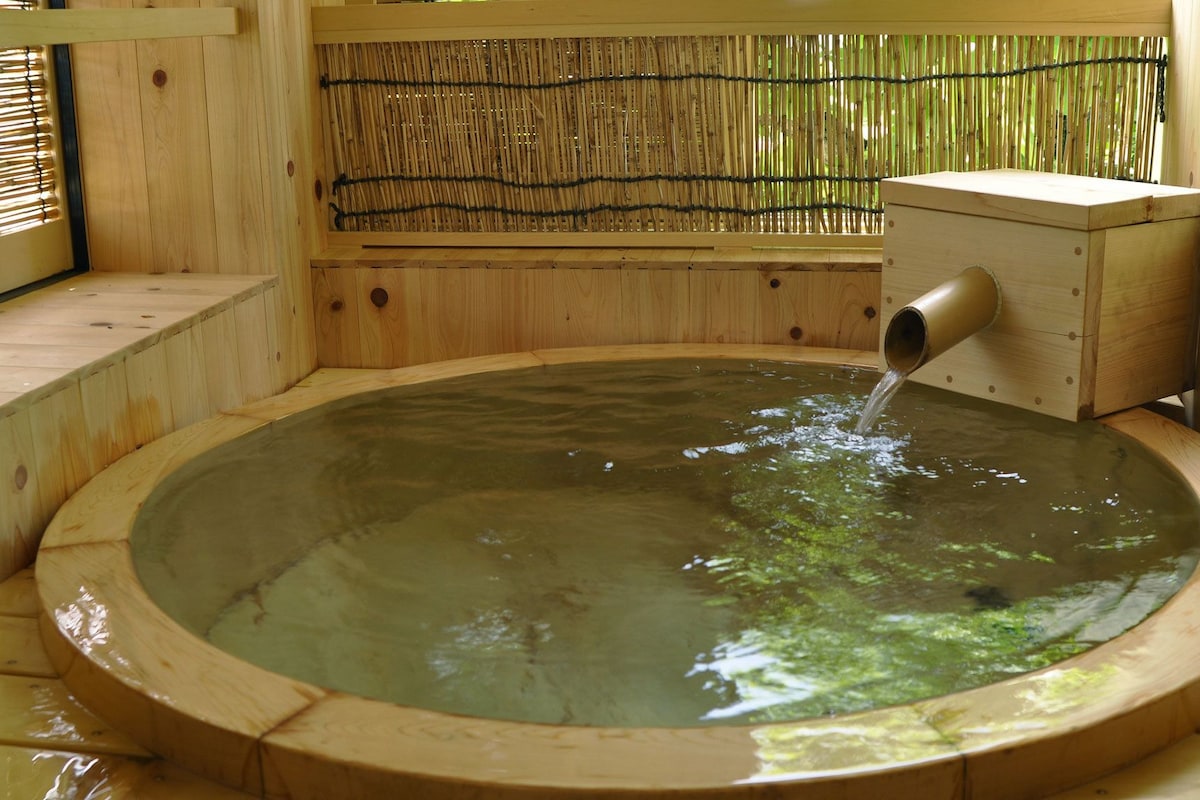 A wooden hot tub with a bamboo backdrop and a water spout.