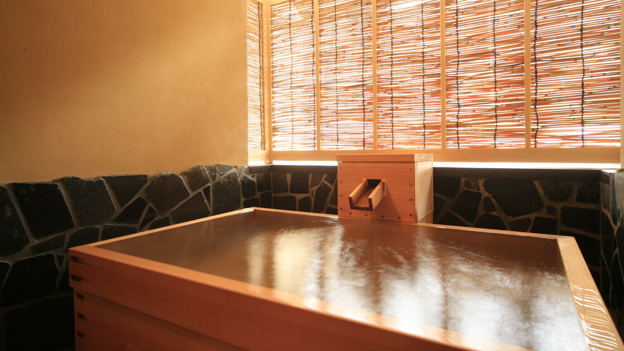 Quarto com paredes de pedra, um banco de madeira e uma mesa de madeira.