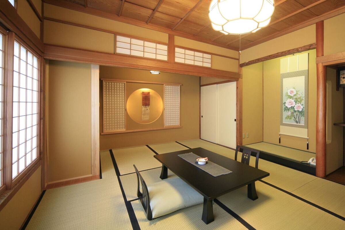 A traditional Japanese room with tatami flooring, a low table, a cushioned bench, sliding doors, and a hanging scroll.