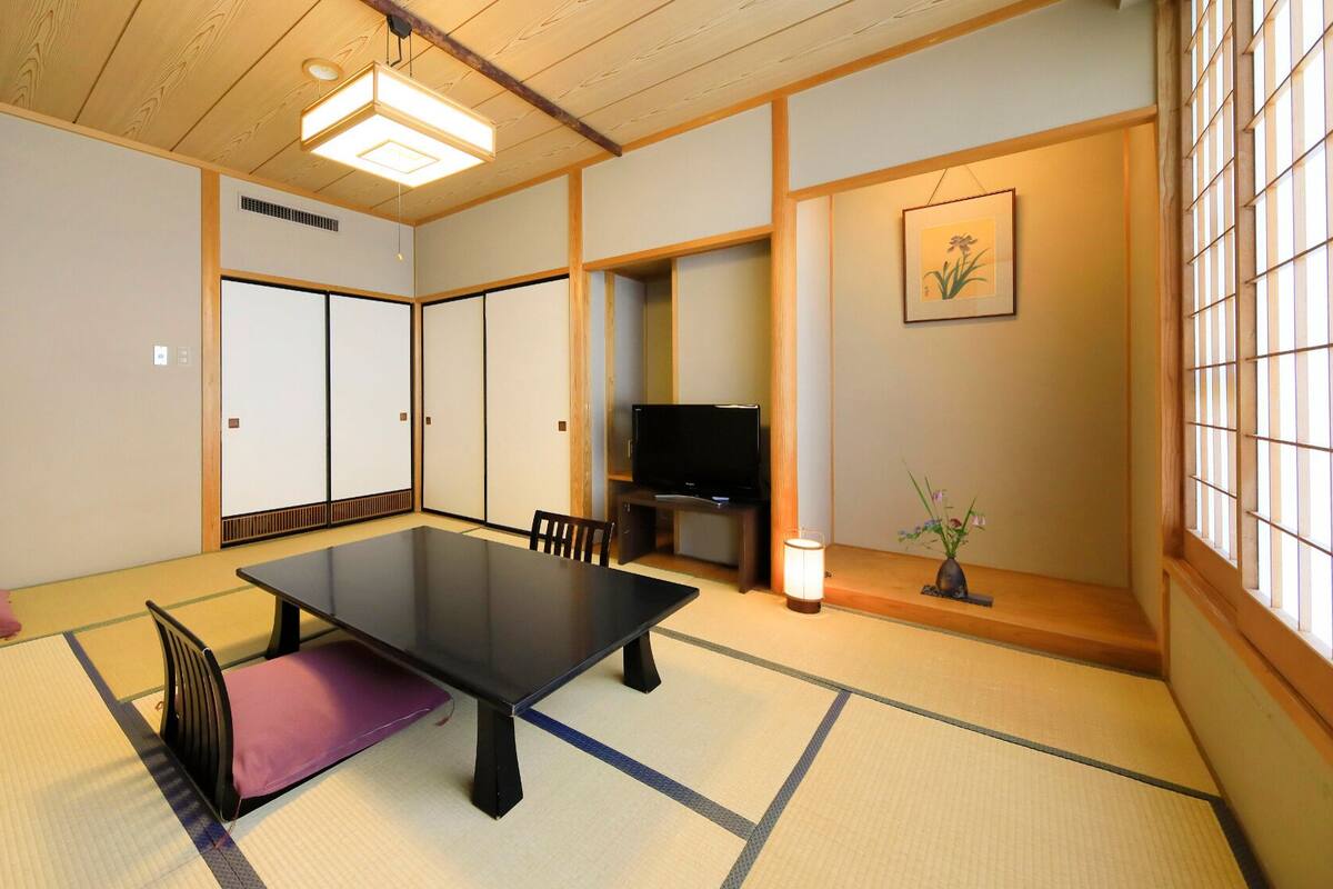 A traditional Japanese room with tatami flooring, a low table, a television, and sliding doors.