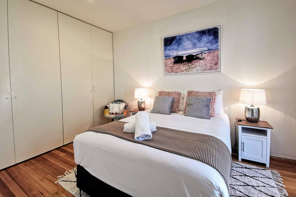 A bedroom with a large bed, two bedside tables with lamps, a wardrobe, and a framed picture on the wall.